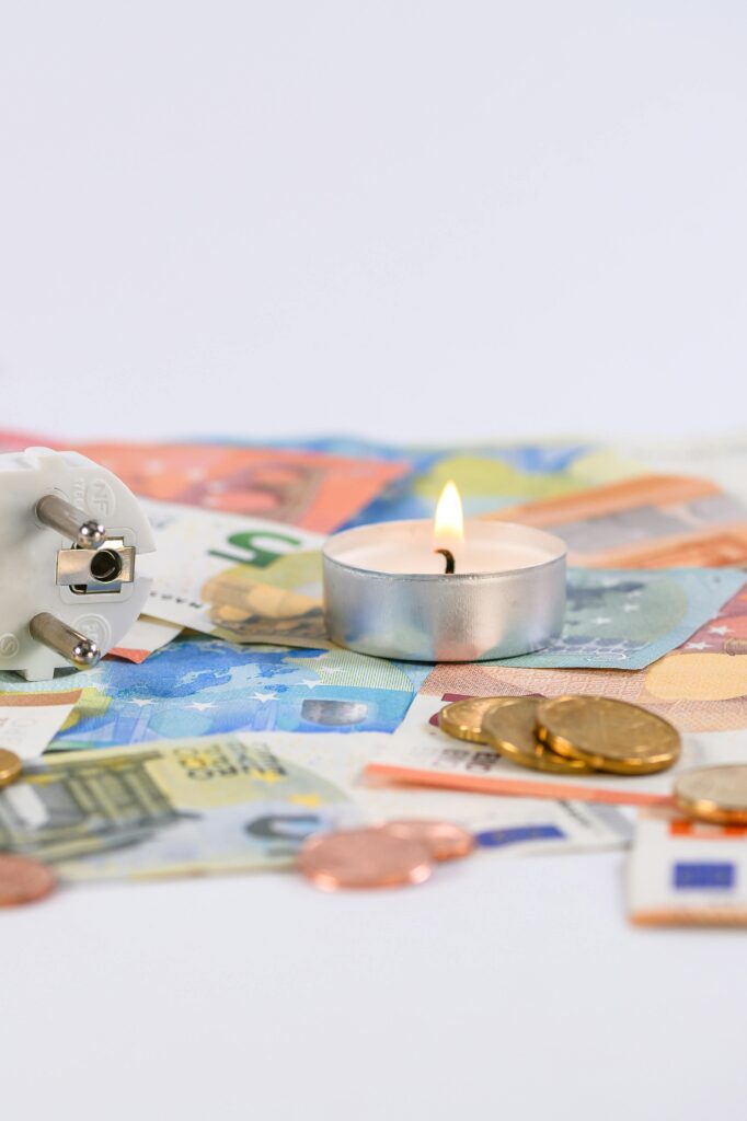 A burning candle on Euro money with a power plug symbolizing energy costs.